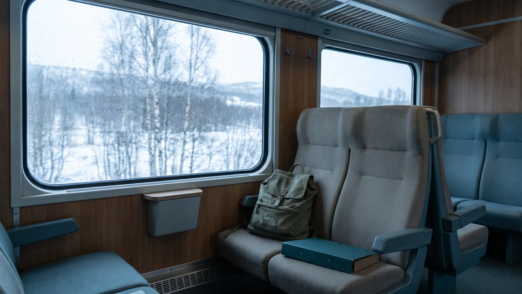Tågkupé med ryggsäck och mapp, vinterlandskap utanför fönstret.